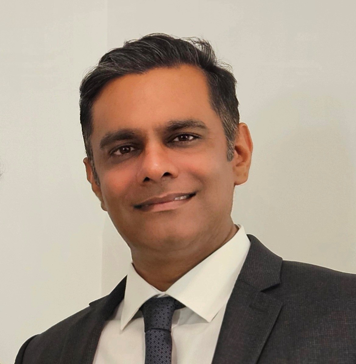 A smiling man in a suit and tie against a plain light-colored background.