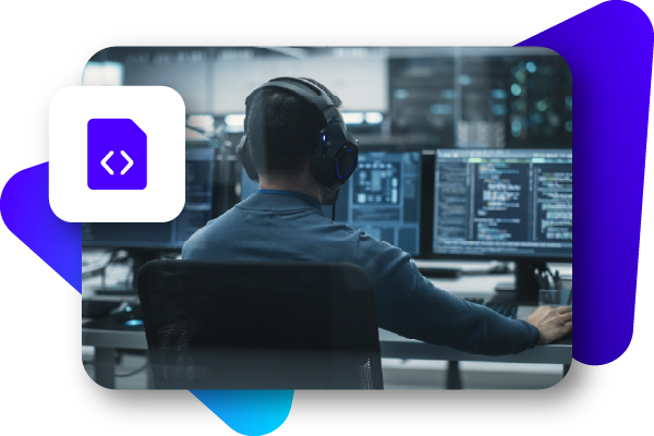 A person with headphones sits at a desk, working on multiple computer screens displaying code and data.