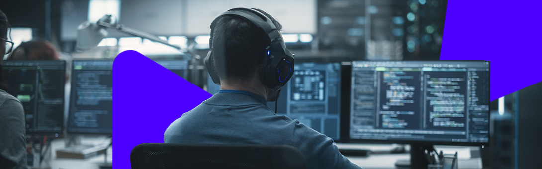 A person wearing headphones working at a desk with multiple monitors showing code and data.