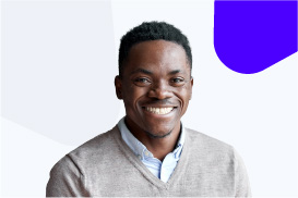 A smiling man with short black hair wearing a gray sweater and a collared shirt against a white background.