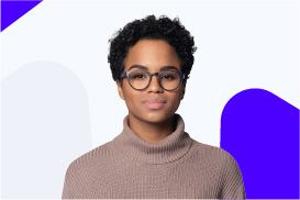 A young woman with short curly hair and glasses, wearing a beige turtleneck sweater, standing against a light background with blue accents.