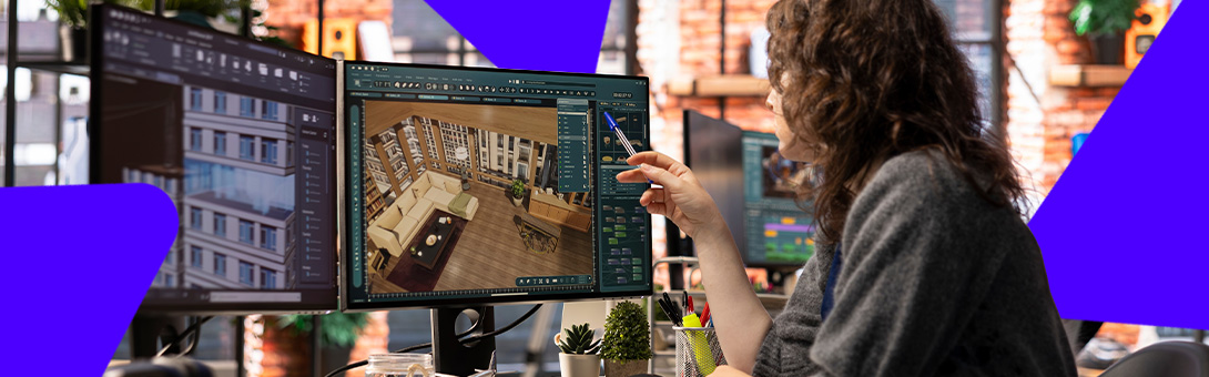 A woman with curly hair using a tablet outdoors, with monitors displaying 3D models in front of her.